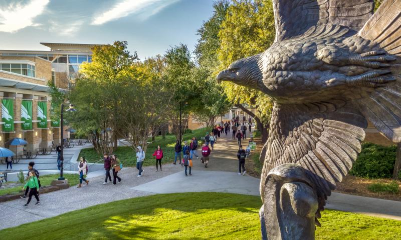 Students walking around campus with an eagle statue to the right